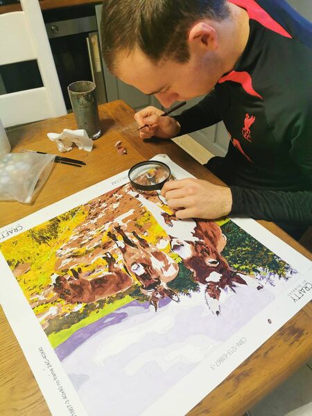 Jack working on one of the paintings with a magnifying glass.
