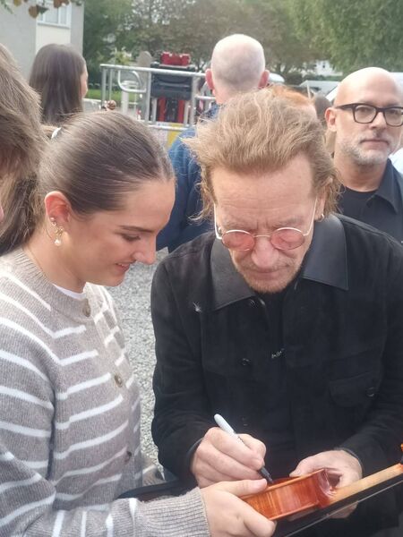 Bono signing Hilary's fiddle after performing with U2 at their old school, Mount Temple in Dublin, to mark the 50th anniversary of their first ever gig 